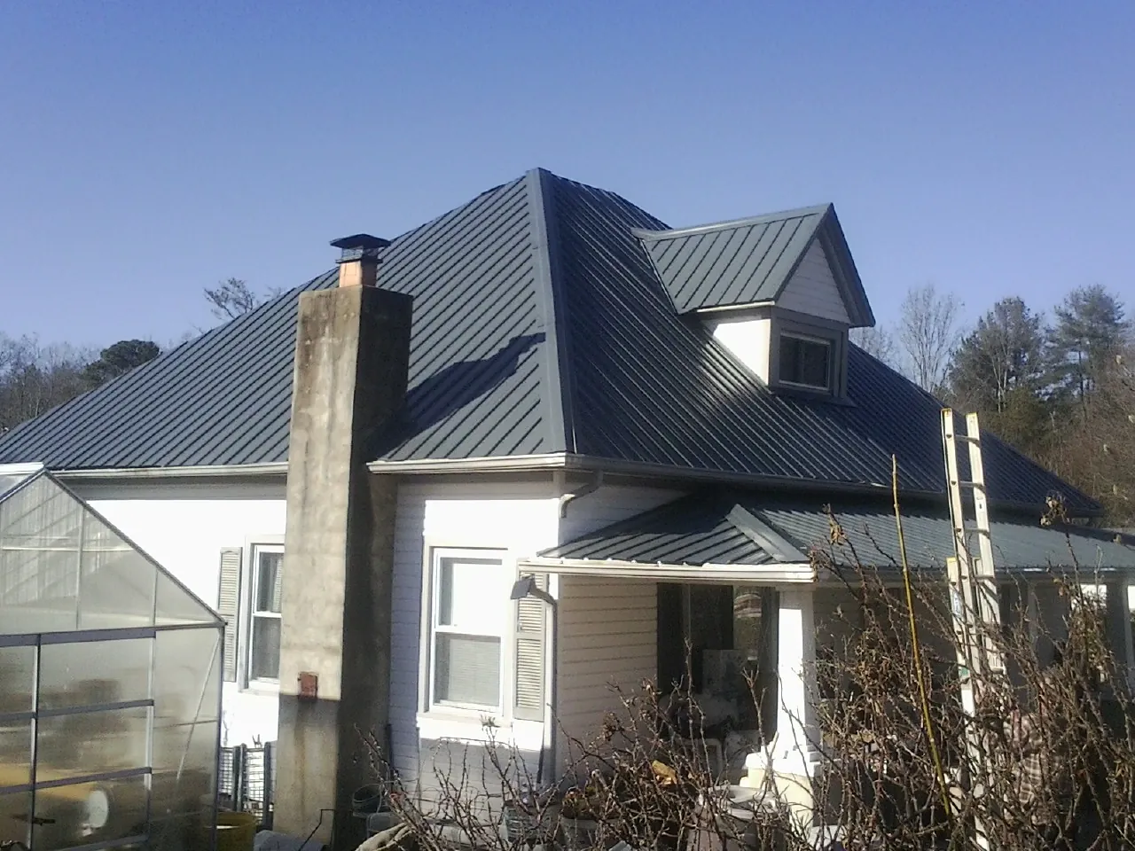 Dark blue standing seam metal roof on a white farmhouse with dormer — Slate & Tile Roof Repair by Roofing Brothers in Central Village