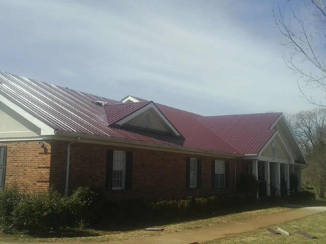 Red metal roof with gabled entries on a long brick building, from a Hail Damage Roof Repair job in Central Village