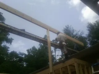 Carpenter setting a ridge beam over a new addition frame in Central Village