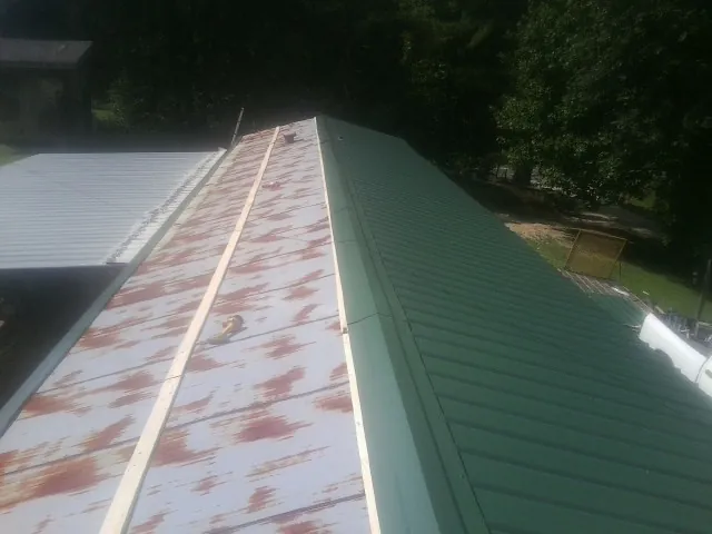 Old rusted panels beside newly installed green metal roofing — Wind Damage Roof Repair by Roofing Brothers in Central Village