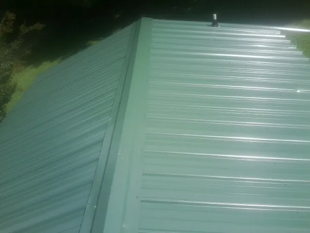 New green metal panels meeting at the ridge of a roof — Flat Roof Repair work by our crew in Central Village