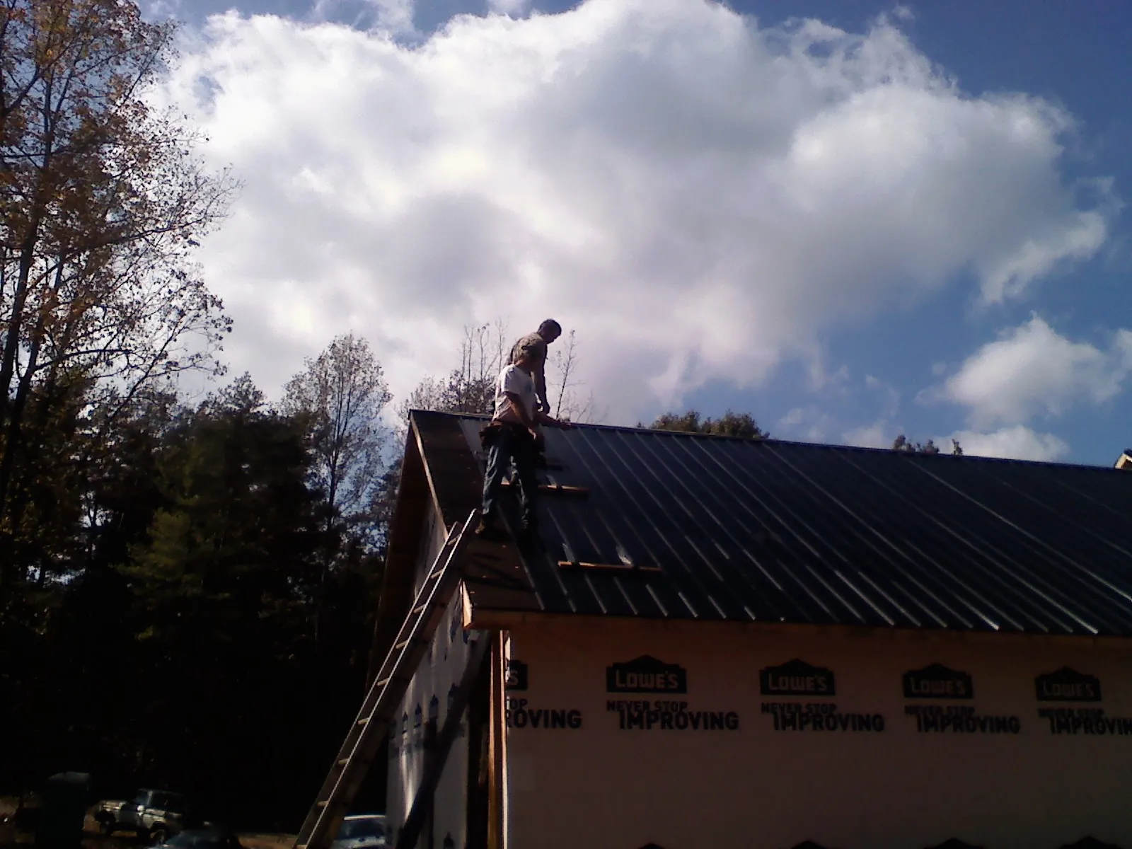 Roofer fastening dark metal panels high against a cloudy sky, from a Roof Inspection job in Central Village