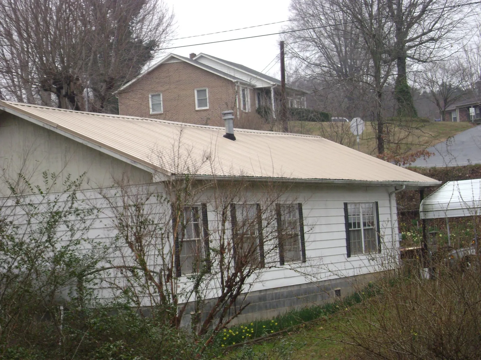 Tan metal roof on a white sided house set into a hillside — Commercial Roofing by Roofing Brothers in Central Village