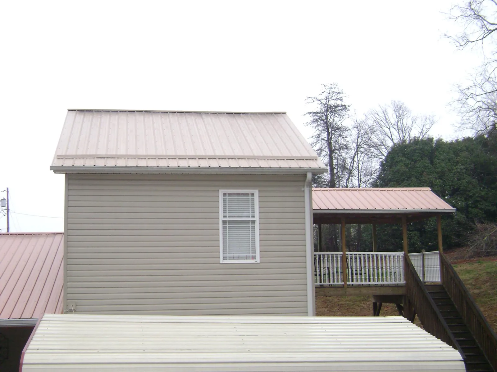 Tan metal roofs on a two story addition and attached porch, from a Roof Replacement job in Central Village